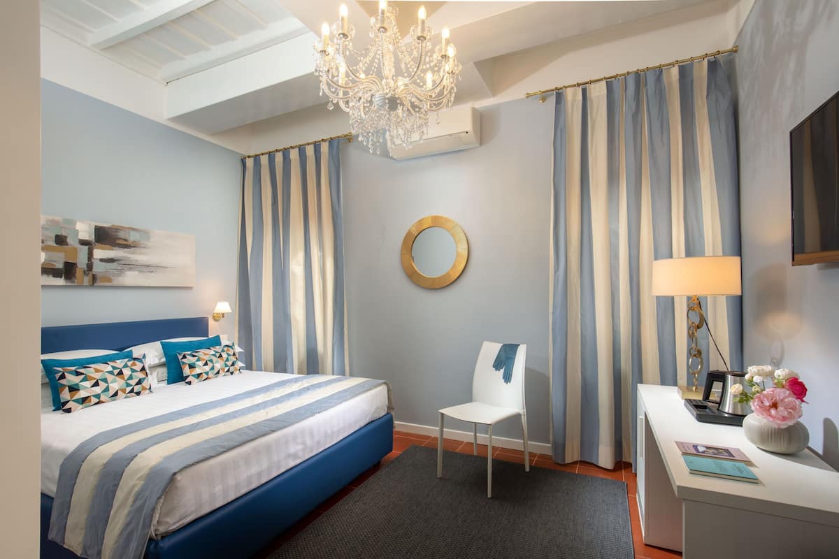 A bedroom with a bed, a chair, a desk, a chandelier, and curtains.