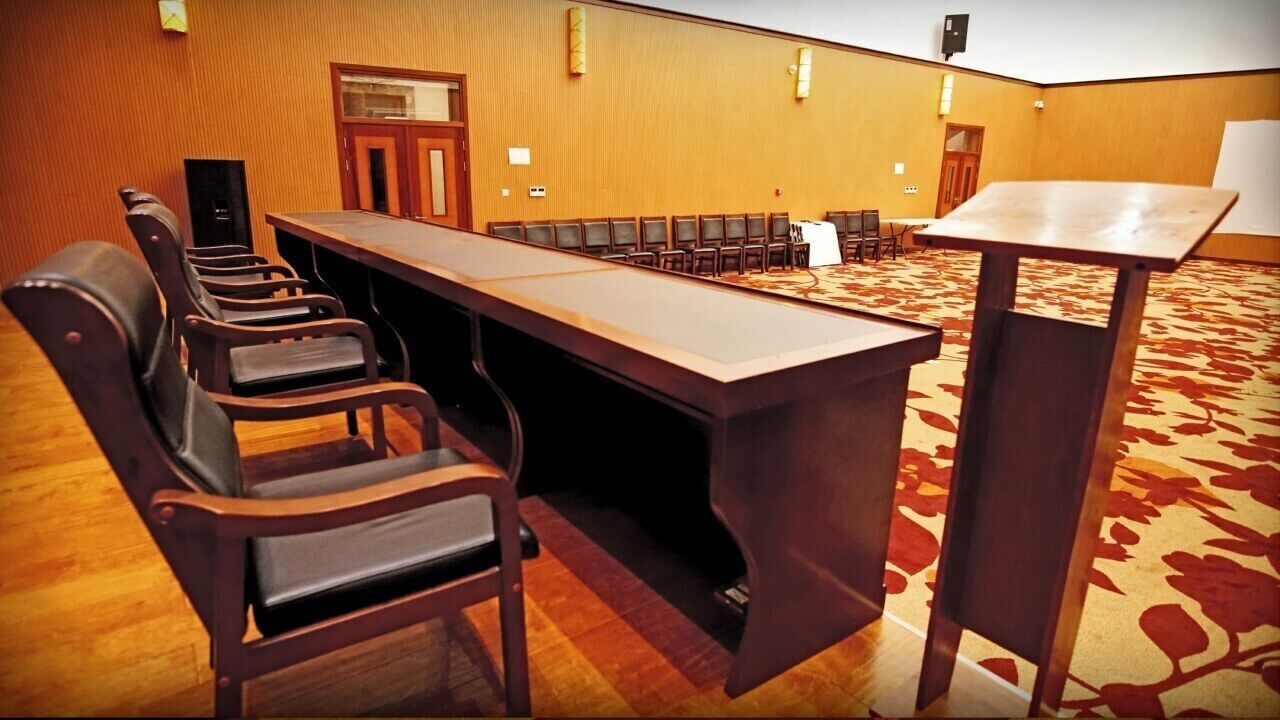 Un salón de conferencias con una larga mesa, varias sillas, un atril y suelo alfombrado.