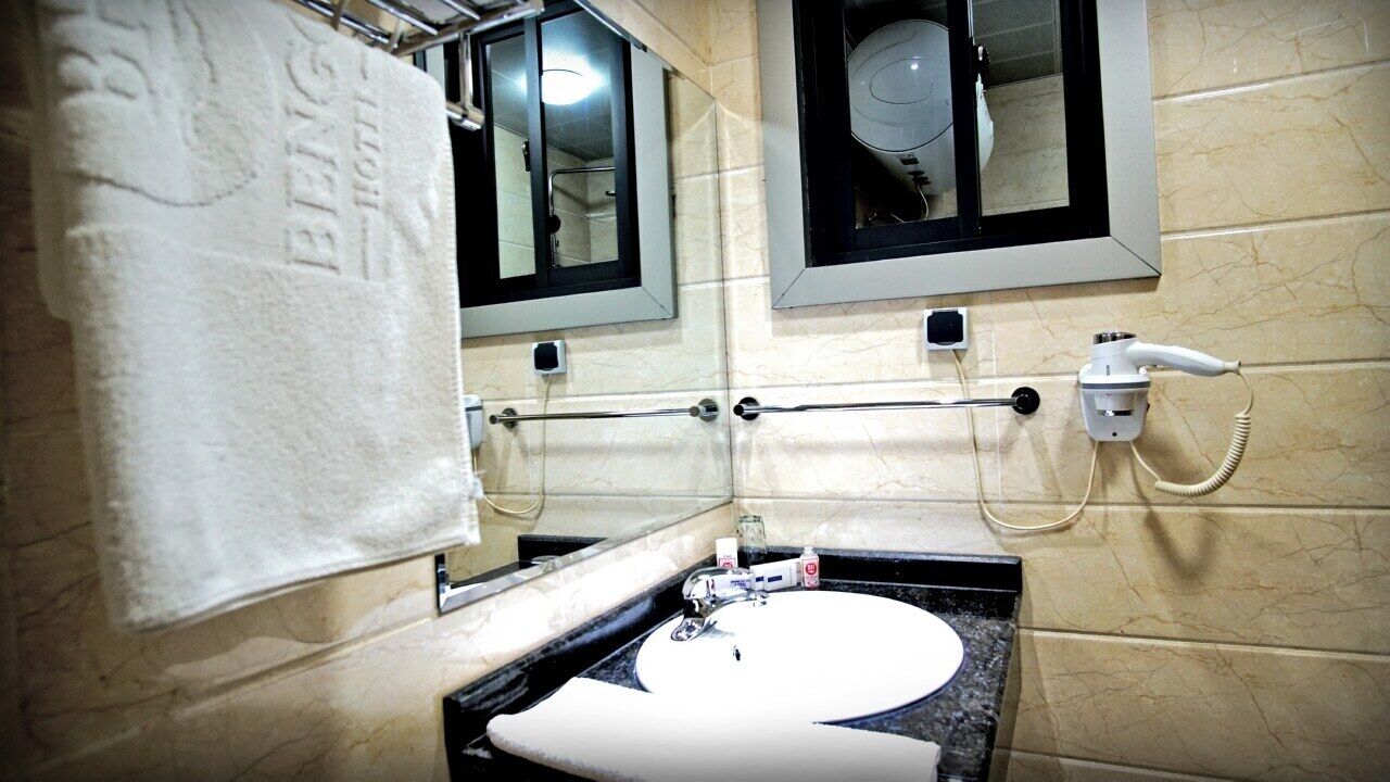 A bathroom with a white sink, a towel hanging on a rack, a mirror, and a hairdryer on the wall.