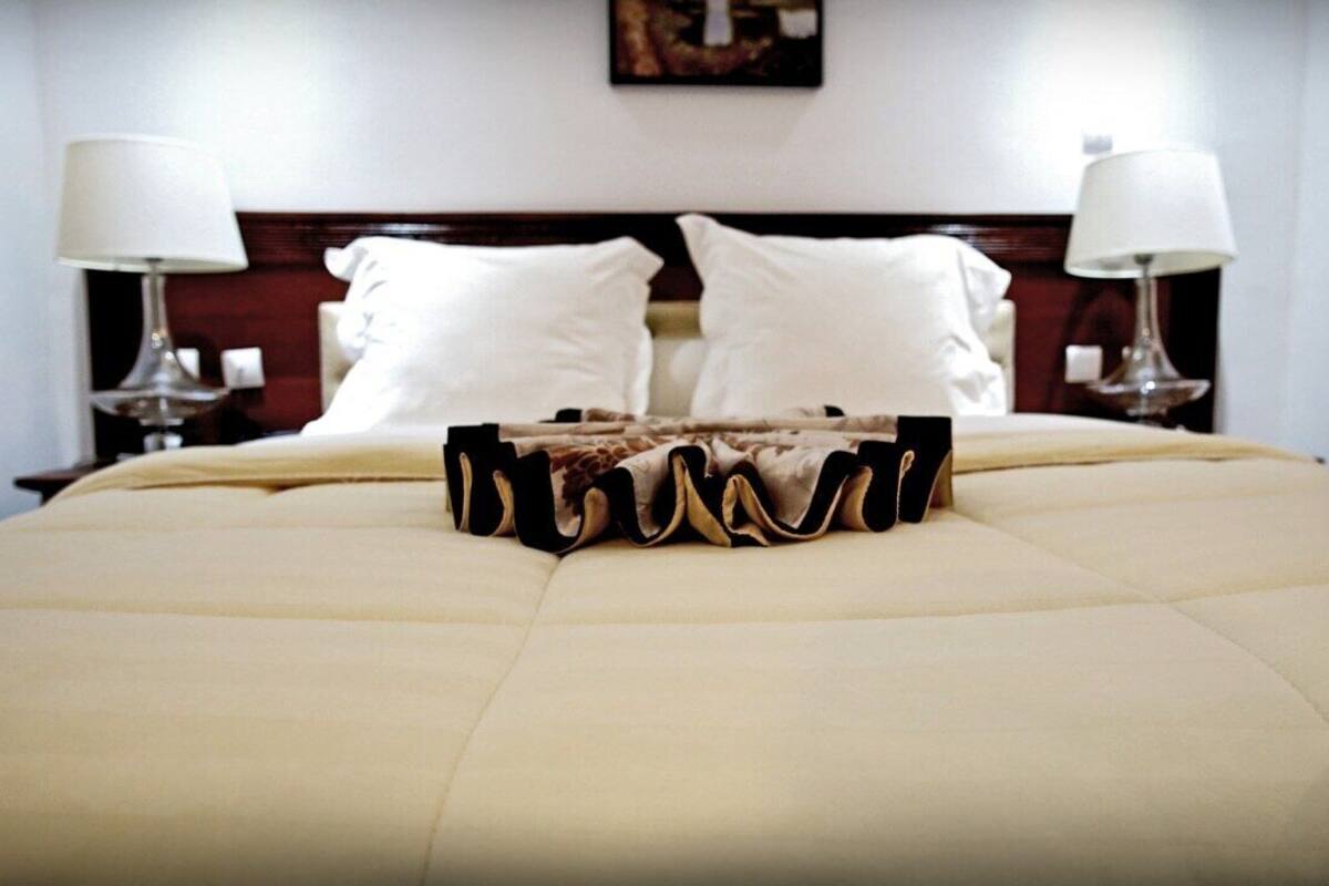 A neatly made bed with a beige duvet, two white pillows, and a decorative wooden headboard.
