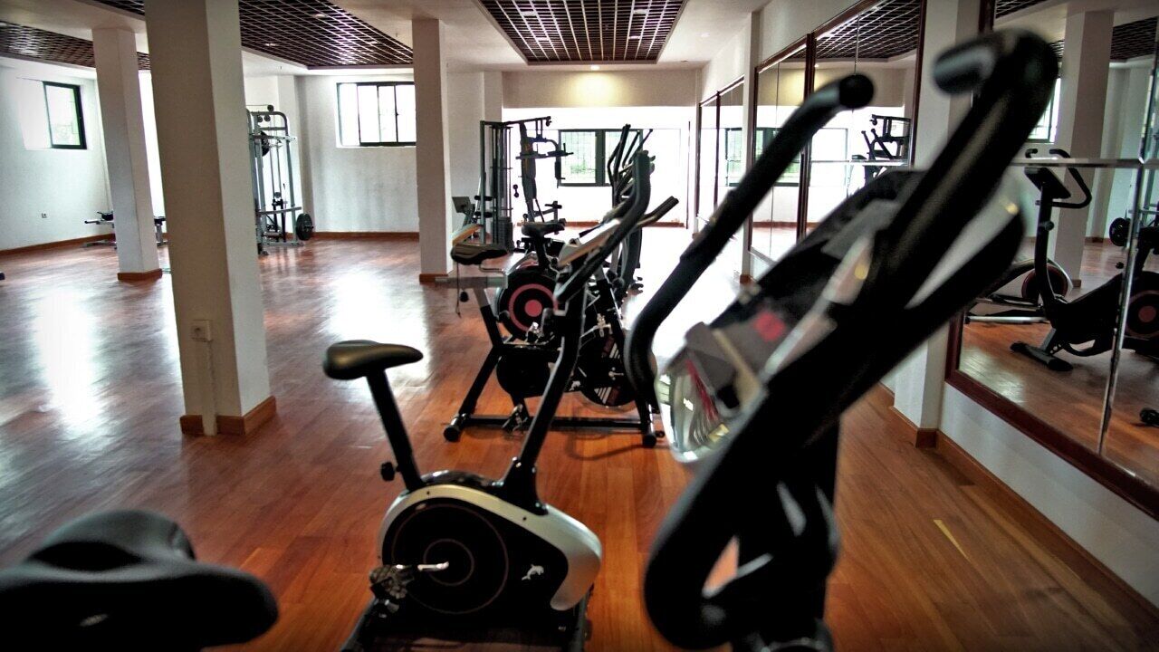 Un gimnasio con equipo de ejercicio, piso de madera y ventanas amplias.
