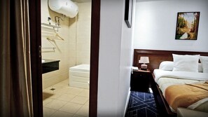 A hotel room with a bed, a nightstand, a painting on the wall, and a bathroom with a sink and towel rack. - BENGO HOTEL (Ebolowa)