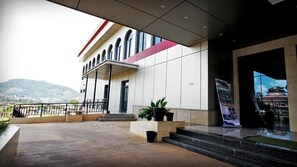 A modern building with a covered entrance, steps leading up to it, and a view of a mountain in the background. - BENGO HOTEL (Ebolowa)