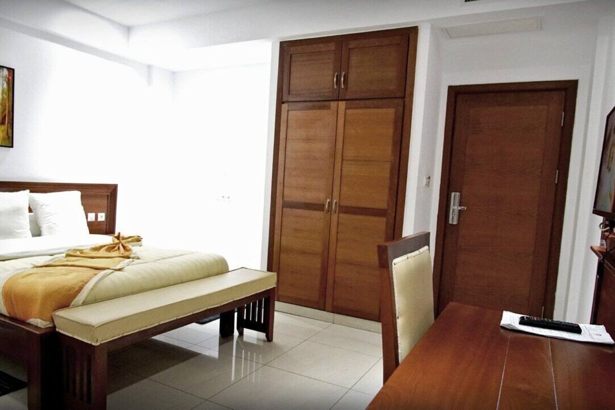 A hotel room with a bed, a bench, a desk, a wardrobe, and a television.