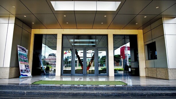 A modern building entrance with glass doors, a green carpet, and a signboard. - BENGO HOTEL (Ebolowa)
