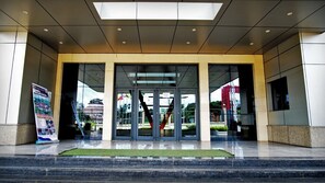 A modern building entrance with glass doors, a green carpet, and a signboard. - BENGO HOTEL (Ebolowa)