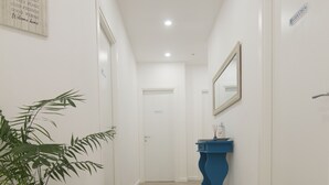 Un pasillo con una planta en maceta, una consola azul y un espejo con marco en la pared.