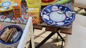 Mesa al aire libre preparada para una comida, con platos, cubiertos y alimentos.