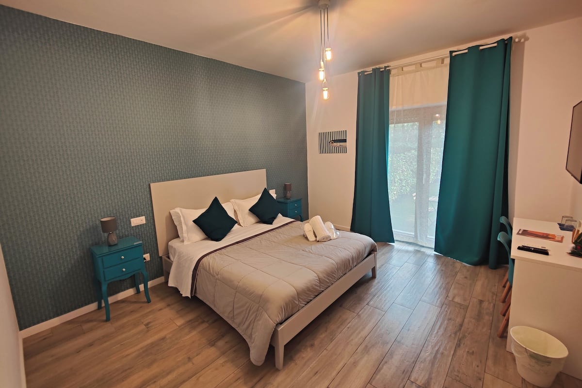 A bedroom with a bed, nightstands, a dresser, and a window with curtains.