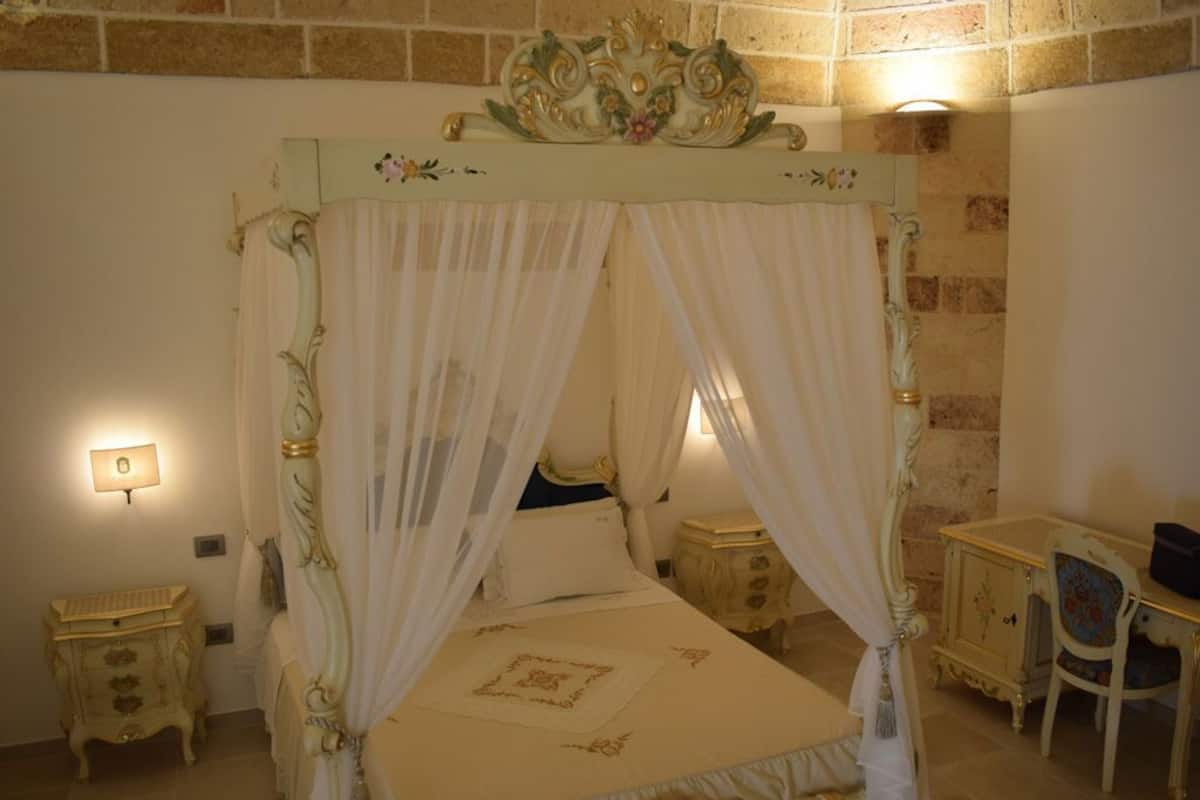 A four-poster bed with a canopy, a bedside table, a chair, and a lamp.