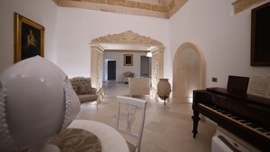 A spacious living room with a grand piano, a white armchair, and a decorative vase. - PlazaCarrisi Hotel & Spa (Cellino San Marco)