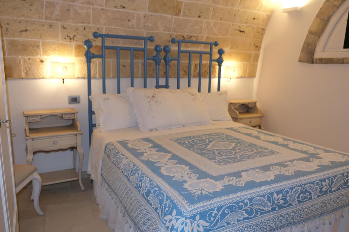 A bedroom with a stone wall, a bed with a blue and white patterned bedspread, two bedside tables, and a nightstand.