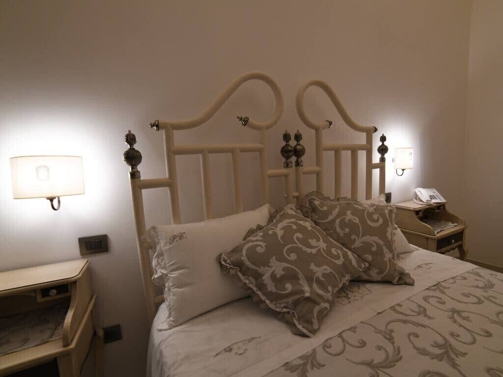 A neatly made bed with a headboard, two bedside tables, and a lamp on the wall.