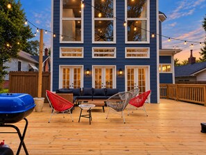 Eine Terrasse mit Gartenmöbeln und Lichterketten vor einem blauen Gebäude.