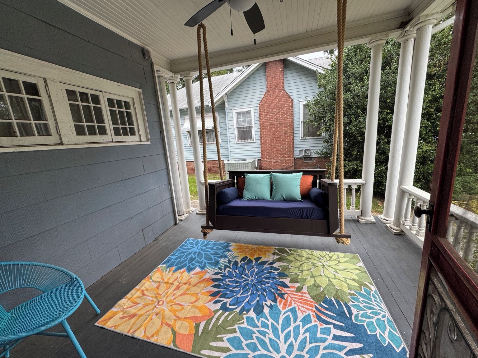 Une véranda avec une balançoire, un tapis coloré et une chaise bleue.