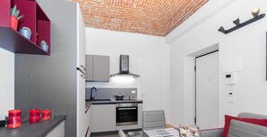 Una cocina compacta con electrodomésticos modernos, un comedor con mesa y sillas, y una pequeña zona de estar con sofá.