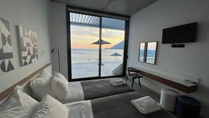 Een hotelkamer met een grote schuifglazen deur naar de oceaan, een bed, een stoel, een televisie en kunstwerken aan de muren.
