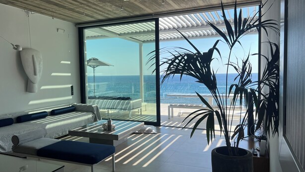 Een moderne kamer met een groot raam met uitzicht op zee, een bank, een bijzettafeltje en een potplant.