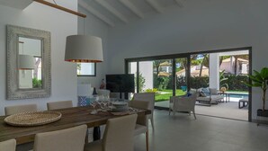 A spacious living area with a dining table, comfortable seating, a flat-screen TV, and a large window offering a view of the outdoors. - Aquamarina.  Large, airy indoor/outdoor living space. 600m from the beach (Conil de la Frontera)
