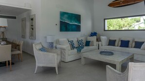 A modern living room with a white sofa set, a coffee table, and a dining area with a wooden table and chairs. - Aquamarina.  Large, airy indoor/outdoor living space. 600m from the beach (Conil de la Frontera)