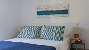 A bedroom with a bed, two pillows, a bedside table with a lamp, and a wall-mounted artwork. - Aquamarina.  Large, airy indoor/outdoor living space. 600m from the beach (Conil de la Frontera)
