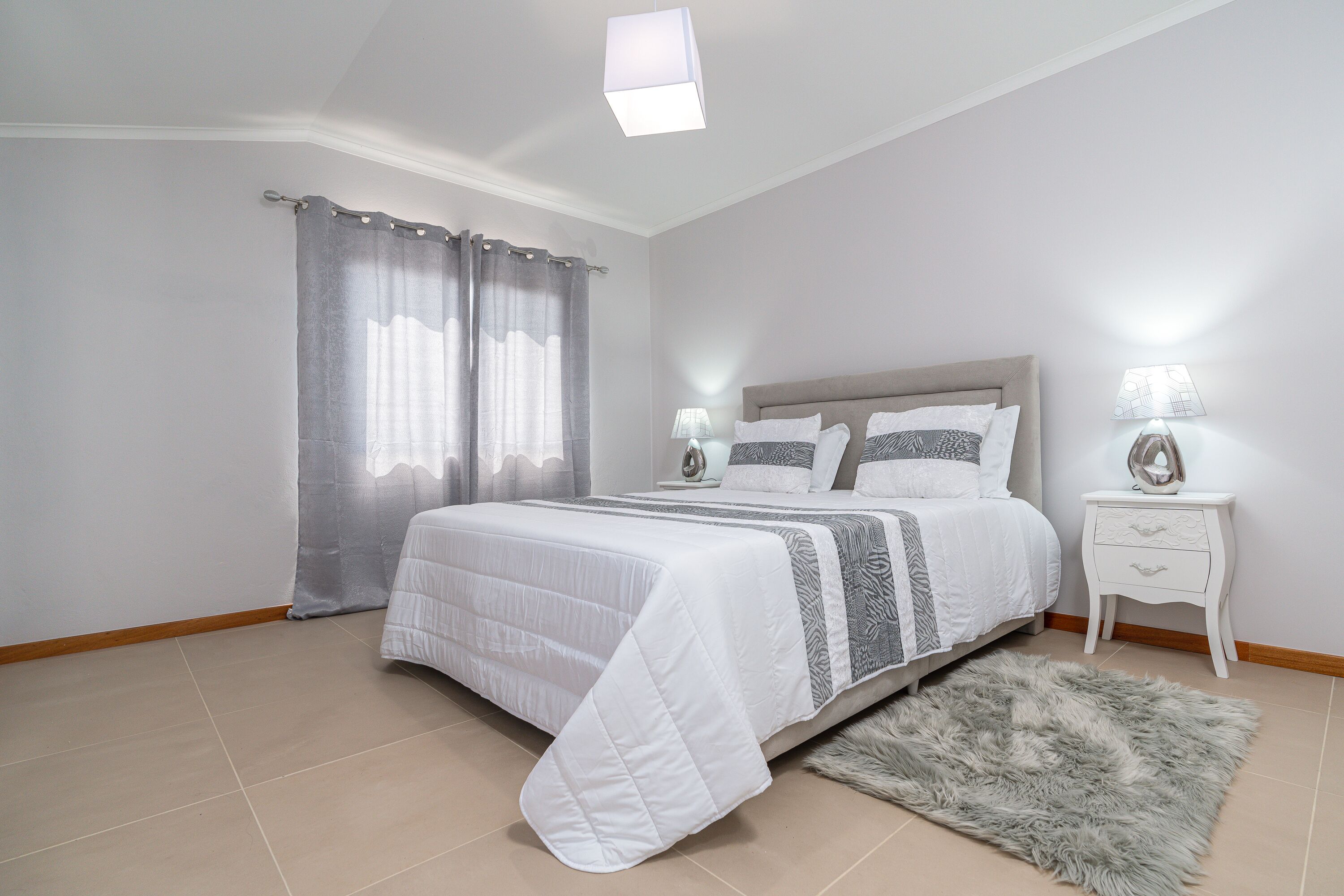 Un dormitorio con cama, cortinas, mesita de noche y alfombra.