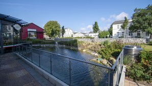 A riverside walkway with a metal railing, a red building, and a stone wall in the background.