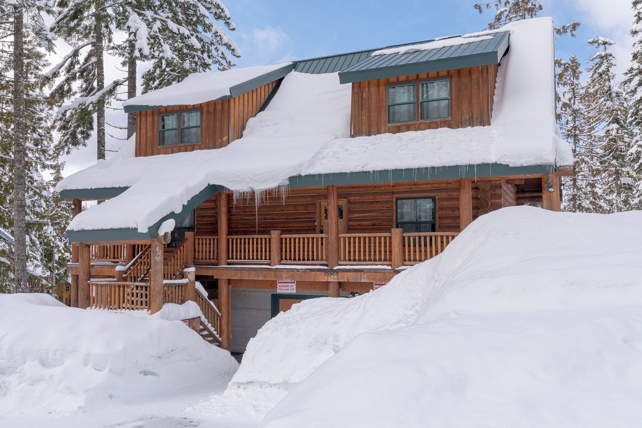 A wooden cabin with a snow-covered roof and a wooden deck.
