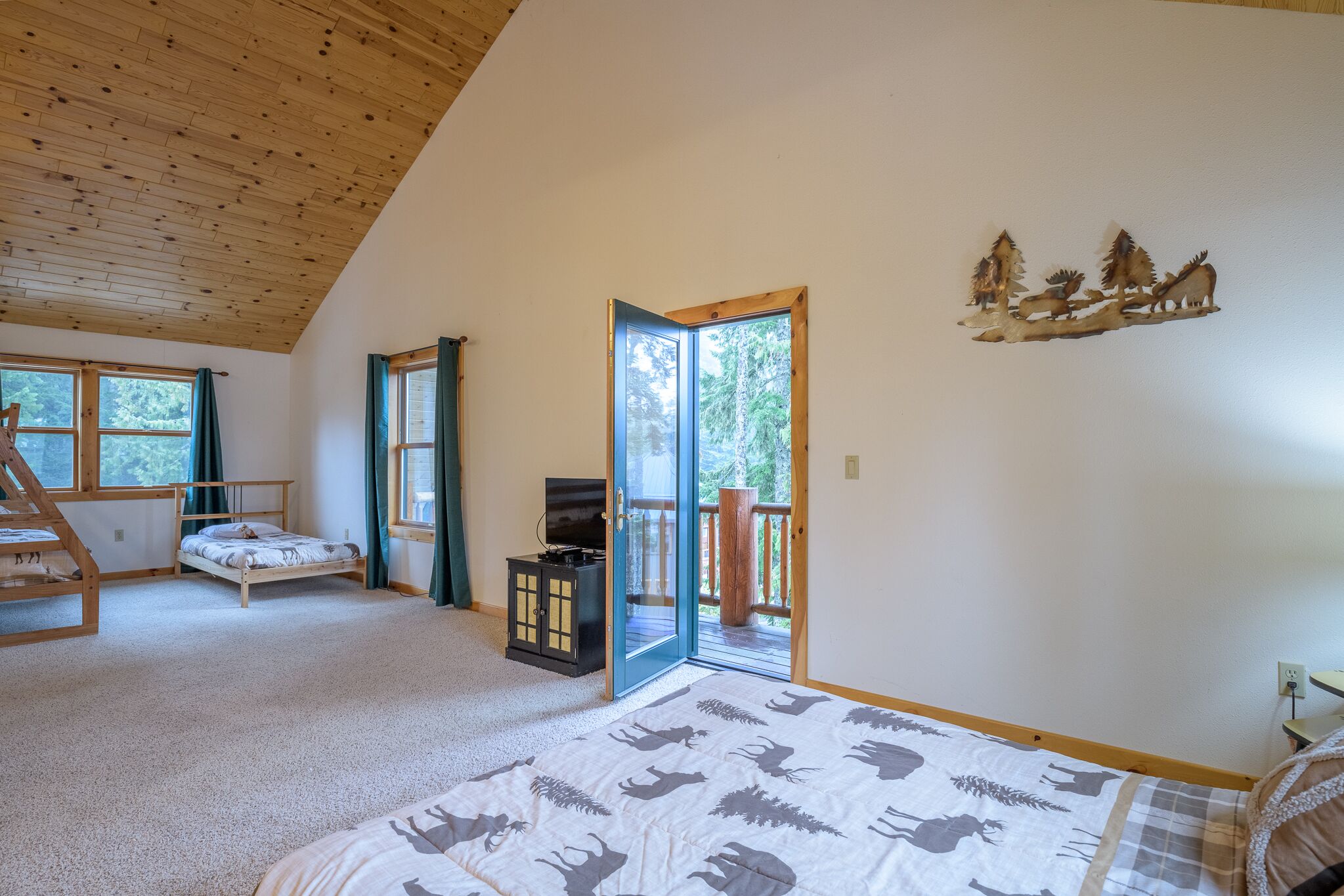 Ein Schlafzimmer mit einem Bett, einem Fernseher, einer Holzboden und einem Balkon mit Blick auf Bäume.