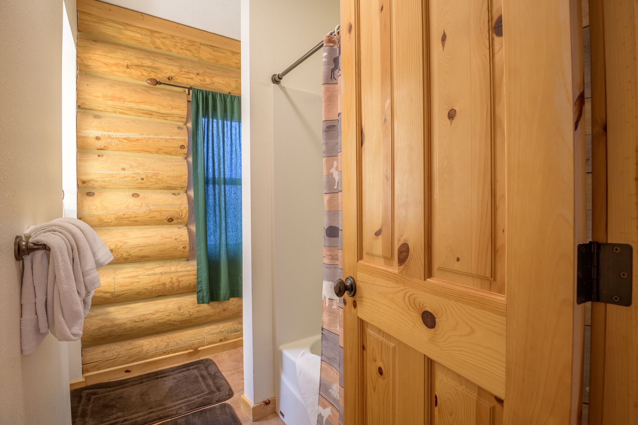 Un baño de cabaña de madera con una bañera, un perchero y una puerta de madera.