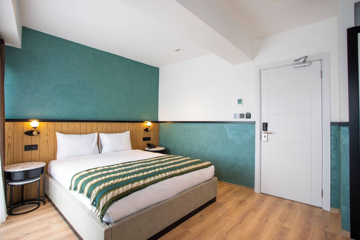 Un dormitorio con cama, mesitas de noche, una mesita auxiliar, una puerta y una lámpara fijada a la pared.