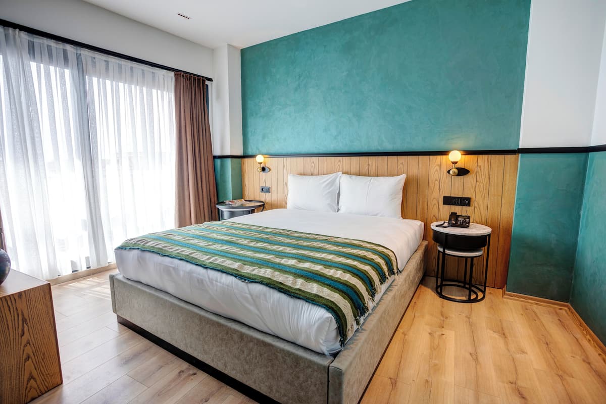 Una habitación de hotel moderna con una cama grande, cabecera de madera y una pared de acento color aguamarina. Hay dos mesitas de noche con lámparas.