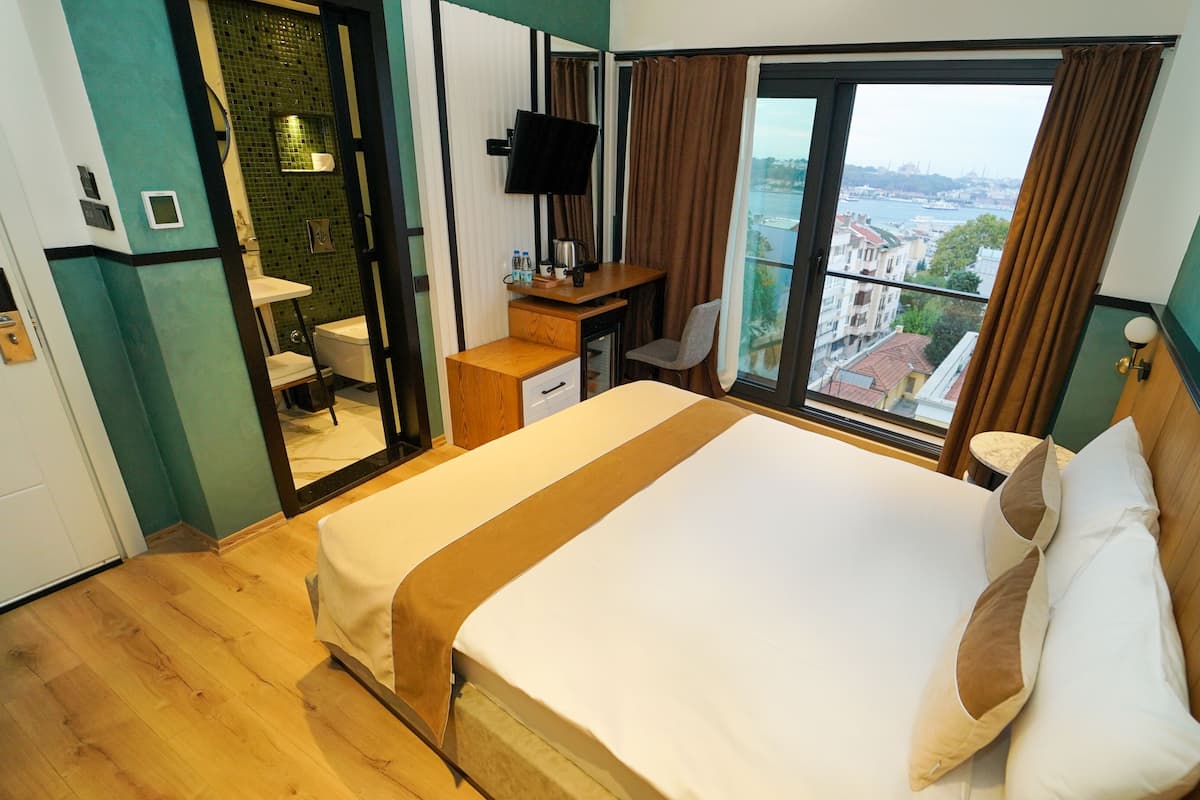 Habitación de hotel con cama, escritorio, silla, televisor y vista a la ciudad.