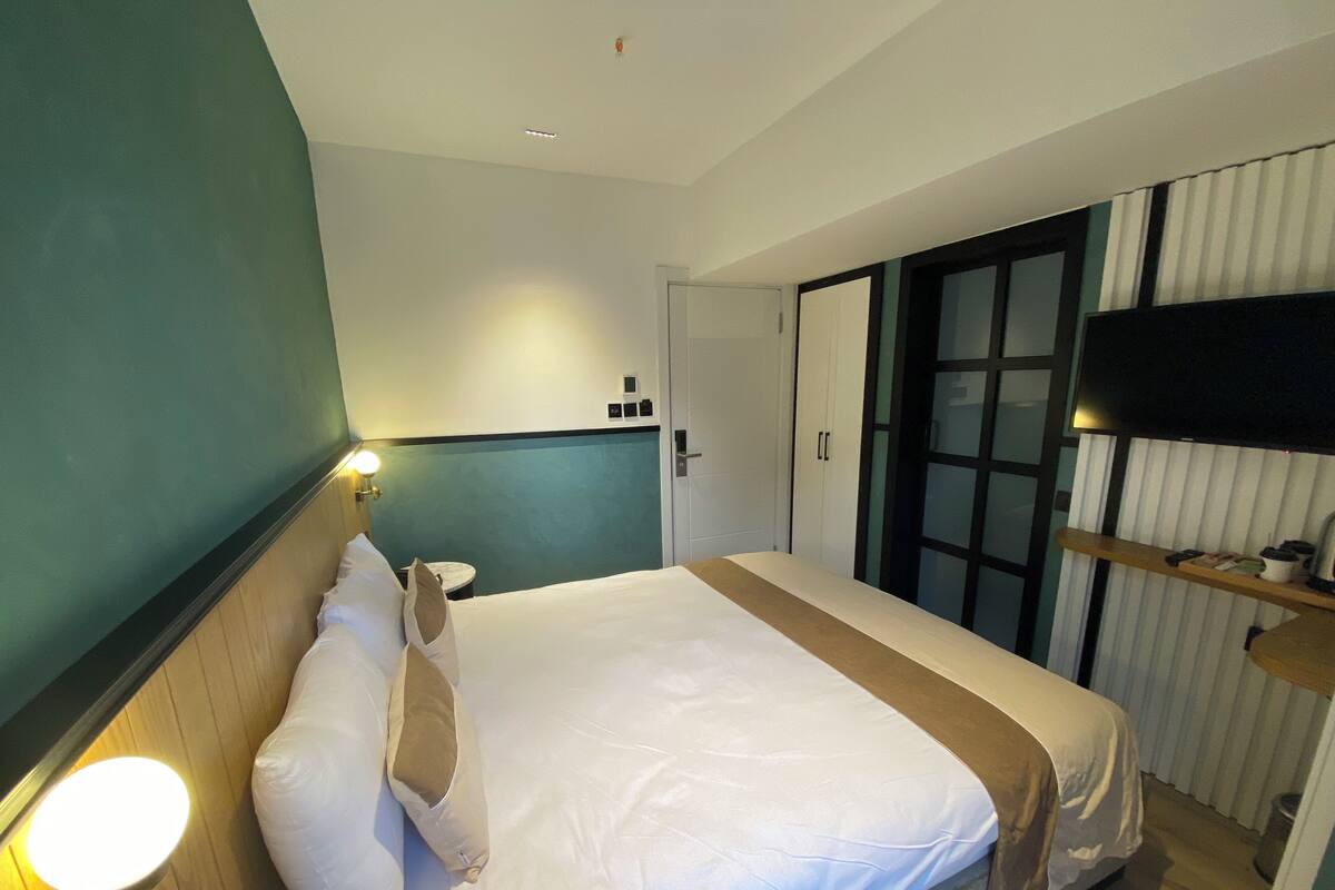 Una habitación de hotel con cama, mesita de noche, lámpara y televisor sobre un mueble.