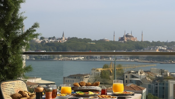 A balcony table with breakfast items and a view of a cityscape with a bridge and a mosque. - Fragments Hotel (Istanbul)