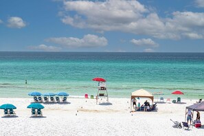 A beach with white sand, clear turquoise water, and a few umbrellas and beach chairs.
