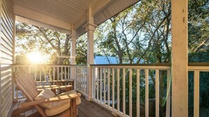 A wooden porch with a white railing, a wooden rocking chair, and a view of trees and a house in the background. - Above the Sea in Old Florida Cottages. South of 30a, Sunset views, Mins to beach (Santa Rosa Beach)