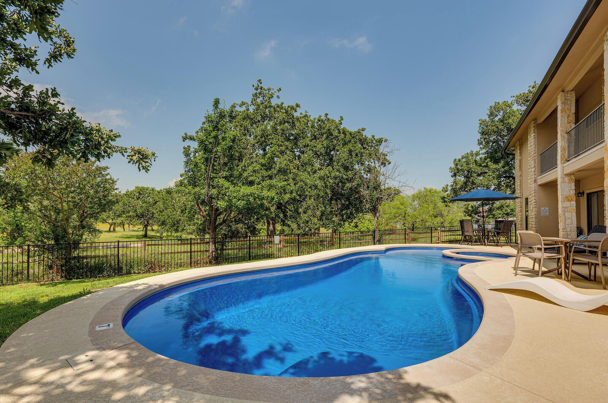 A swimming pool with a curved edge, surrounded by a stone deck and outdoor furniture.