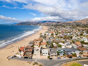 Une zone résidentielle côtière avec des maisons, une plage et des montagnes en arrière-plan.