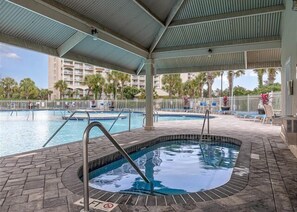 A pool area with a hot tub, lounge chairs, and a covered patio.