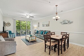 A spacious living room with a dining area, a ceiling fan, and a view through large windows.