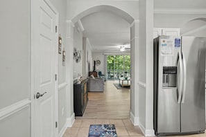 A hallway with a stainless steel refrigerator, a dining area with a table and chairs, and a view of the outdoors.