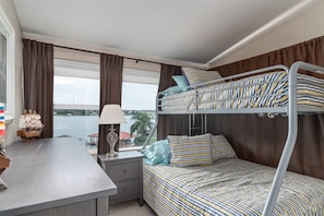 A bunk bed room with a desk, lamp, and a view of a body of water.