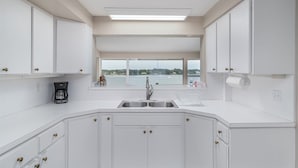 Een moderne keuken met witte kasten, een roestvrijstalen spoelbak en uitzicht op een wateroppervlak door grote ramen.