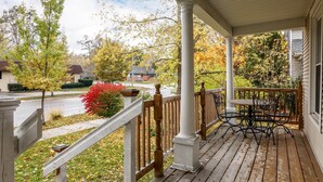 A wooden porch with a railing, a table, and chairs. - Beautiful House | Walk Everywhere | AC| Fire Pit | (Traverse City)