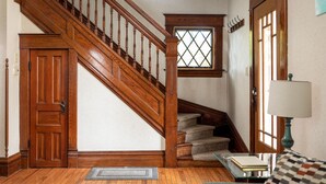 A wooden staircase with a window above it, a door, and a lamp on a table. - Beautiful House | Walk Everywhere | AC| Fire Pit | (Traverse City)
