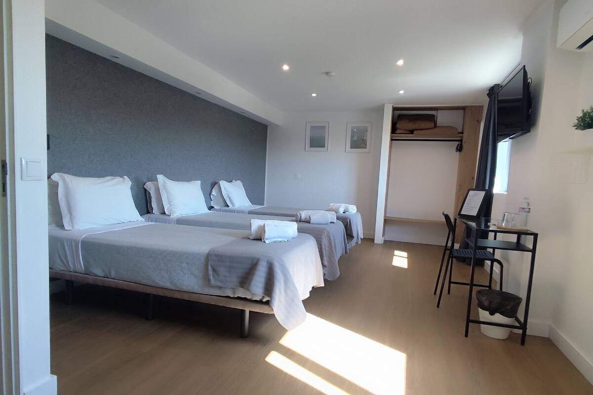 A hotel room with three beds, a desk, a chair, and a television mounted on the wall.