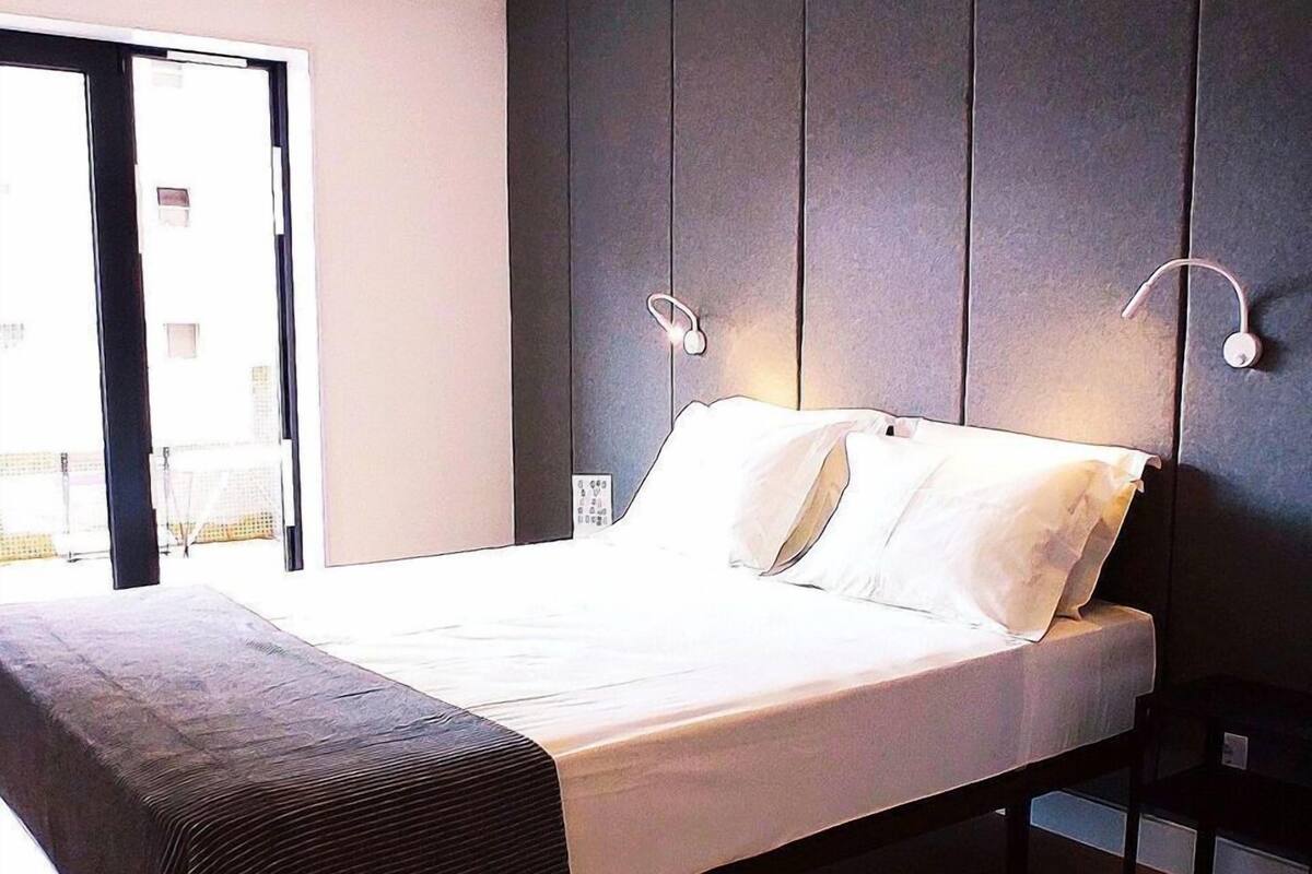 A modern bedroom with a large bed, dark wall paneling, and a wooden floor.