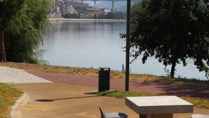 A park bench and picnic table near a river with a bridge in the background. - Residencial Douro (Peso da Régua)