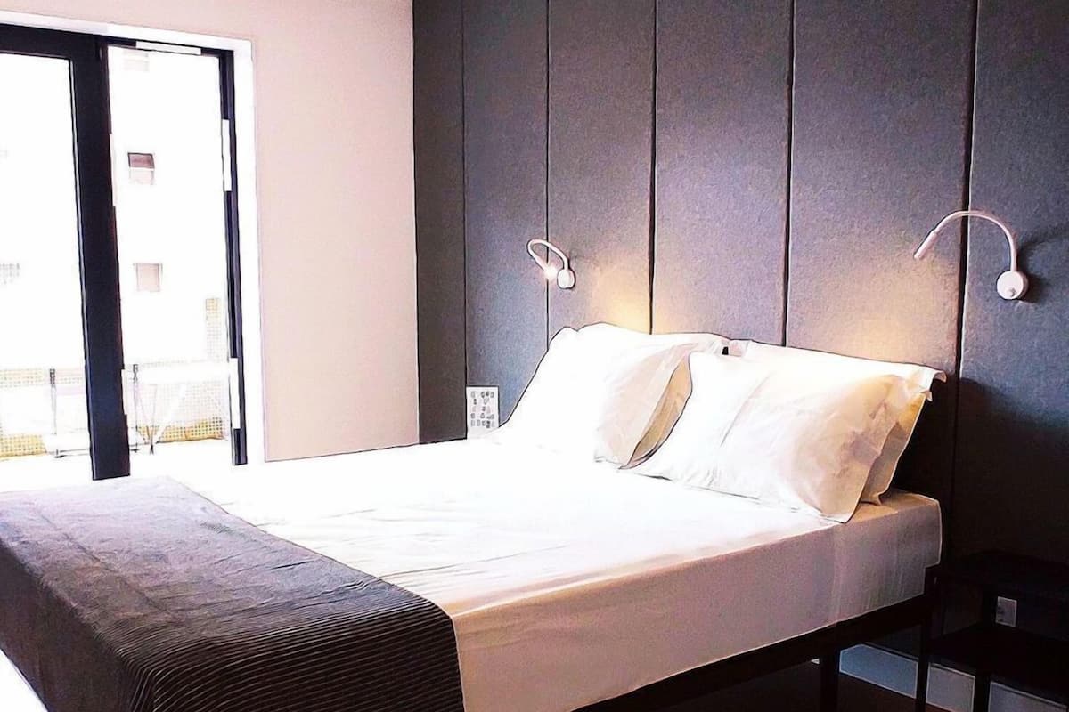 A modern bedroom with a large bed, dark wall paneling, and a wooden floor.